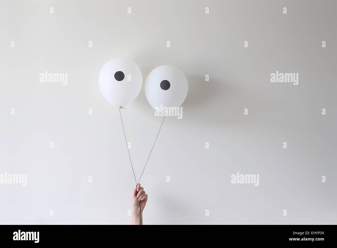 A hand holding a pair of balloons that look like eyes Stock Photo