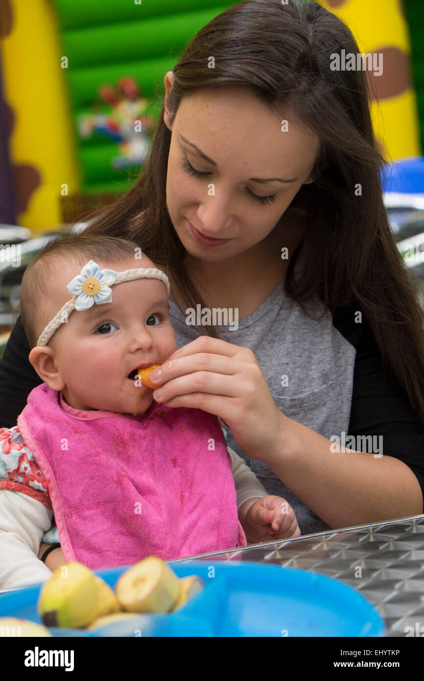 Woman feeding fresh fruit to 8 month old baby girl Stock Photo