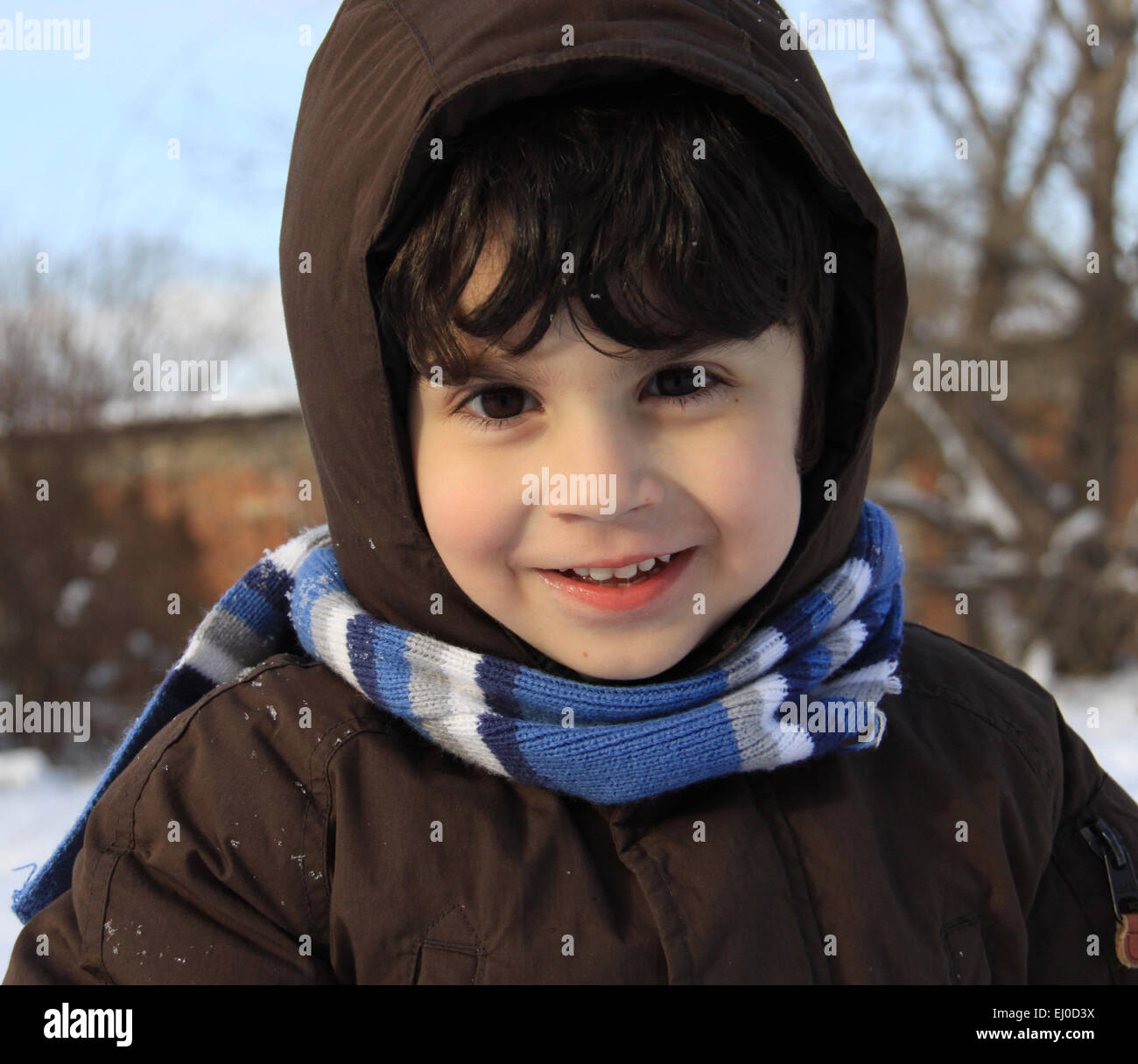 Preschool boy with auburn hair and brown eyes is playing with snow outside in a winter day. He is dressed with warm winter cloth Stock Photo