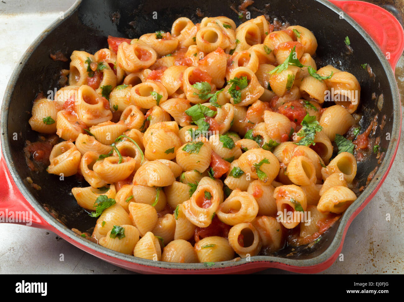 Gomiti elbow pasta shells in arrabbiata tomato, garlic and chili sauce, garnished with chopped parsley, cooking in a frying pan. Stock Photo