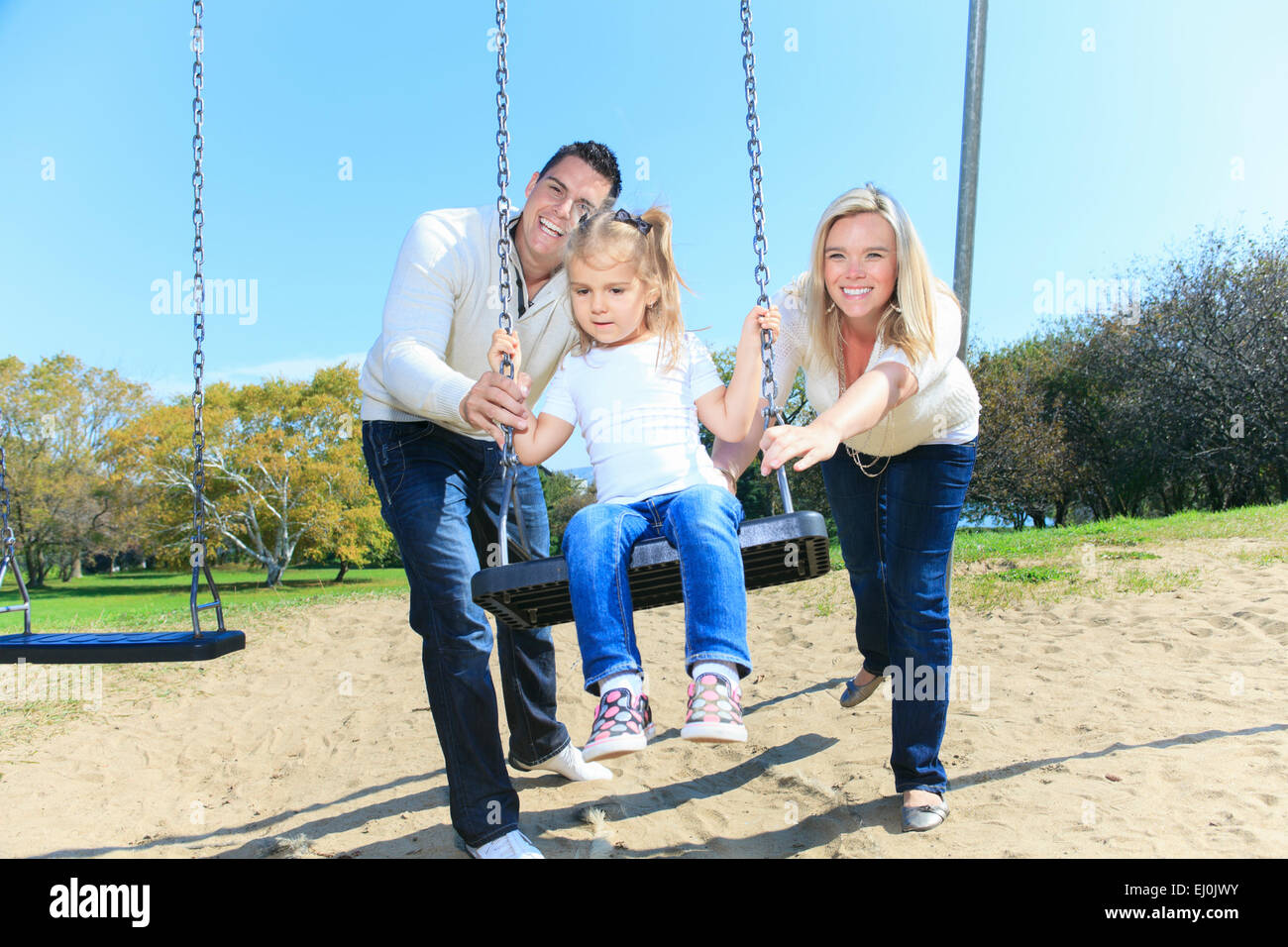 Girl Sitting On A Swing Father On Mother Pushing Stock