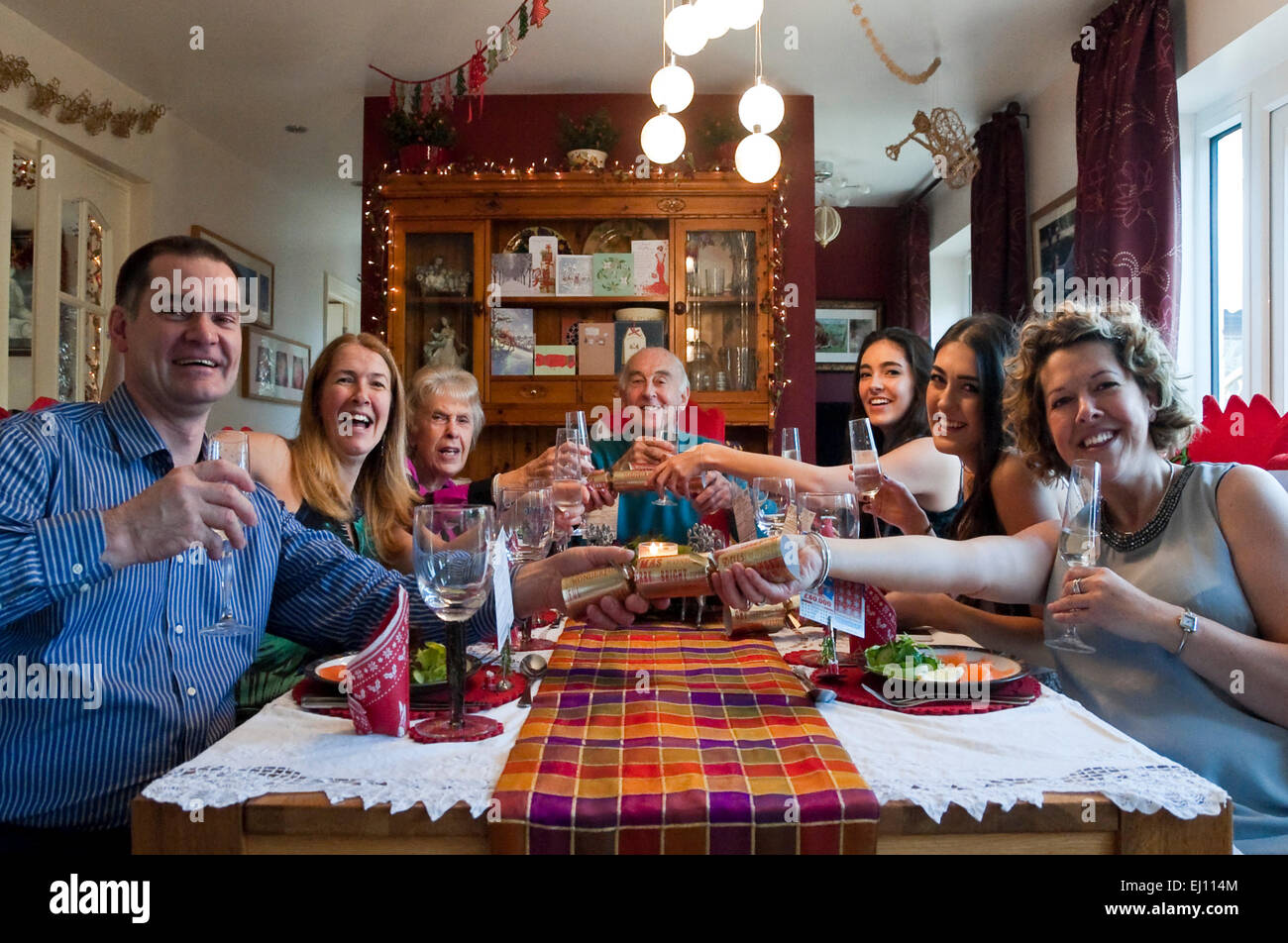 Horizontal view of three generations of a family pulling crackers during Christmas dinner. Stock Photo