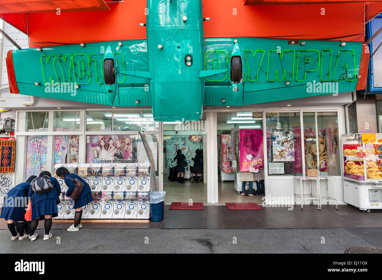 Japanese schoolgirls looking at clothes under a shop sign made from a light aircraft, in the Sanjo shopping arcade in Kyoto, Japan Stock Photo