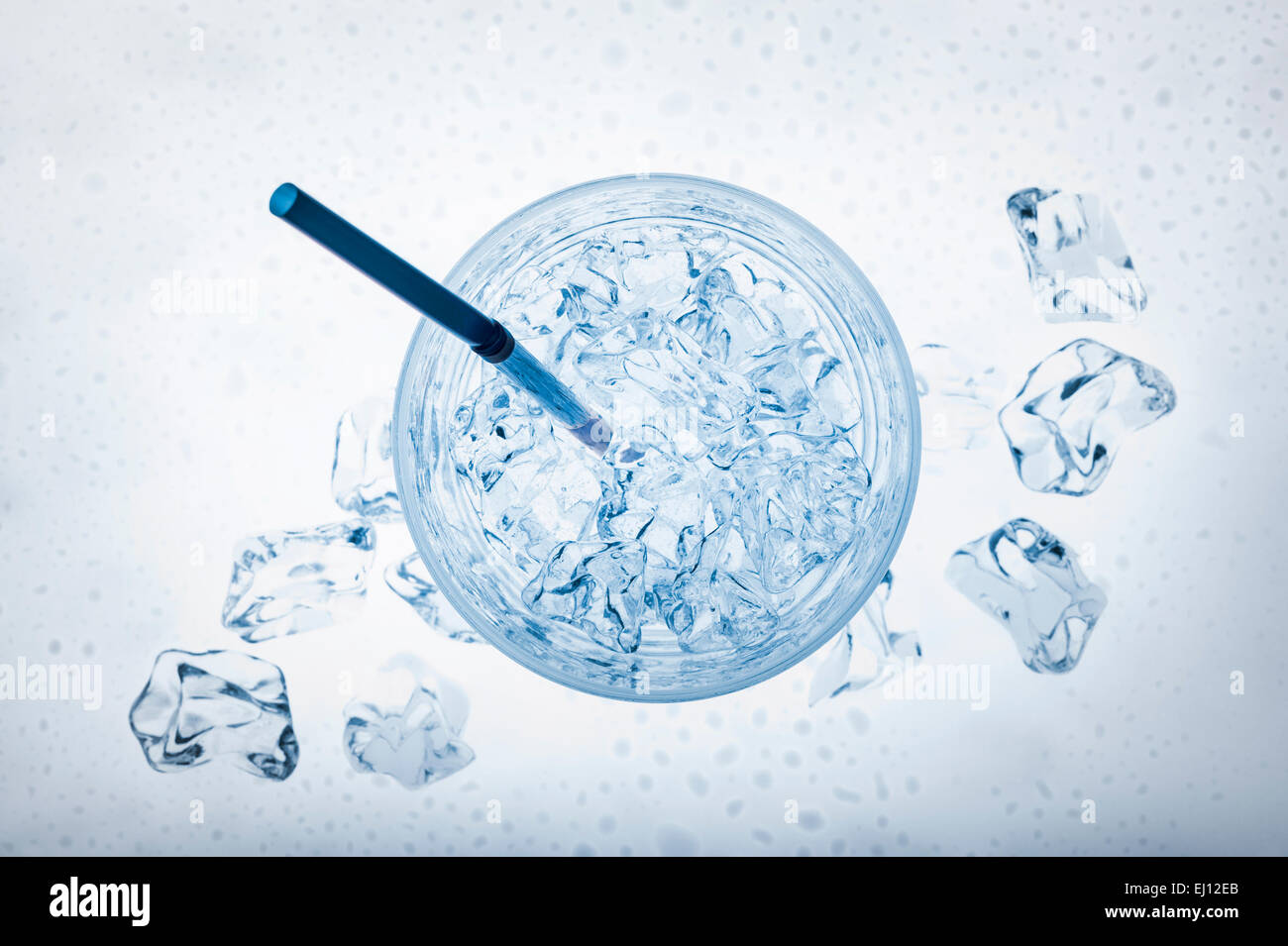 glass full of fresh water with ice cubes and thin cane, on blue background Stock Photo
