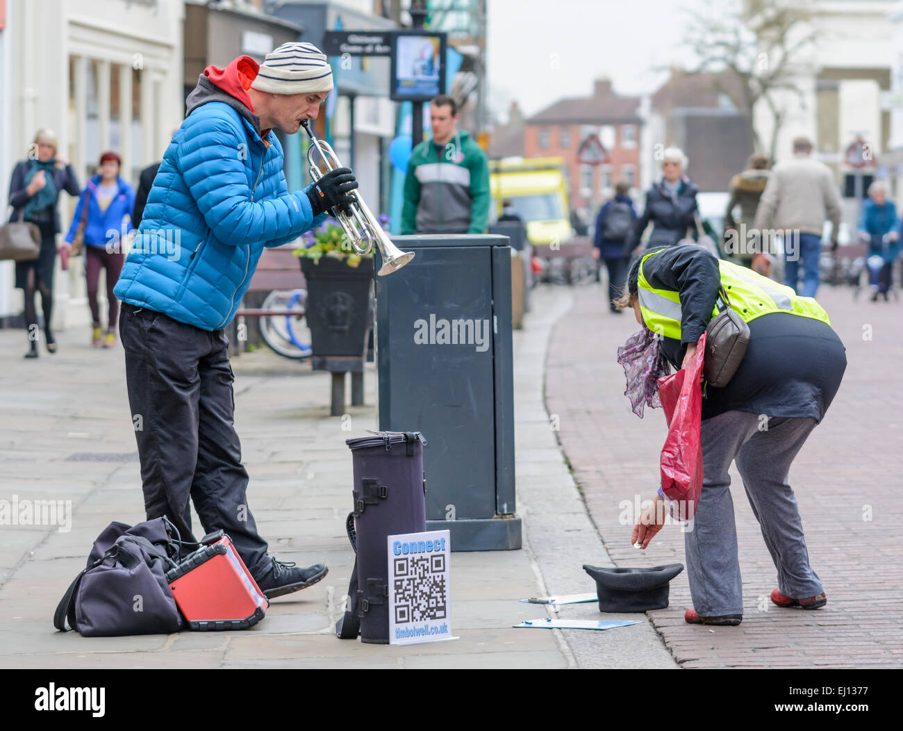 Busker playing the trumpet as a lady puts change in his hat, and he bows to thank her. Stock Photo