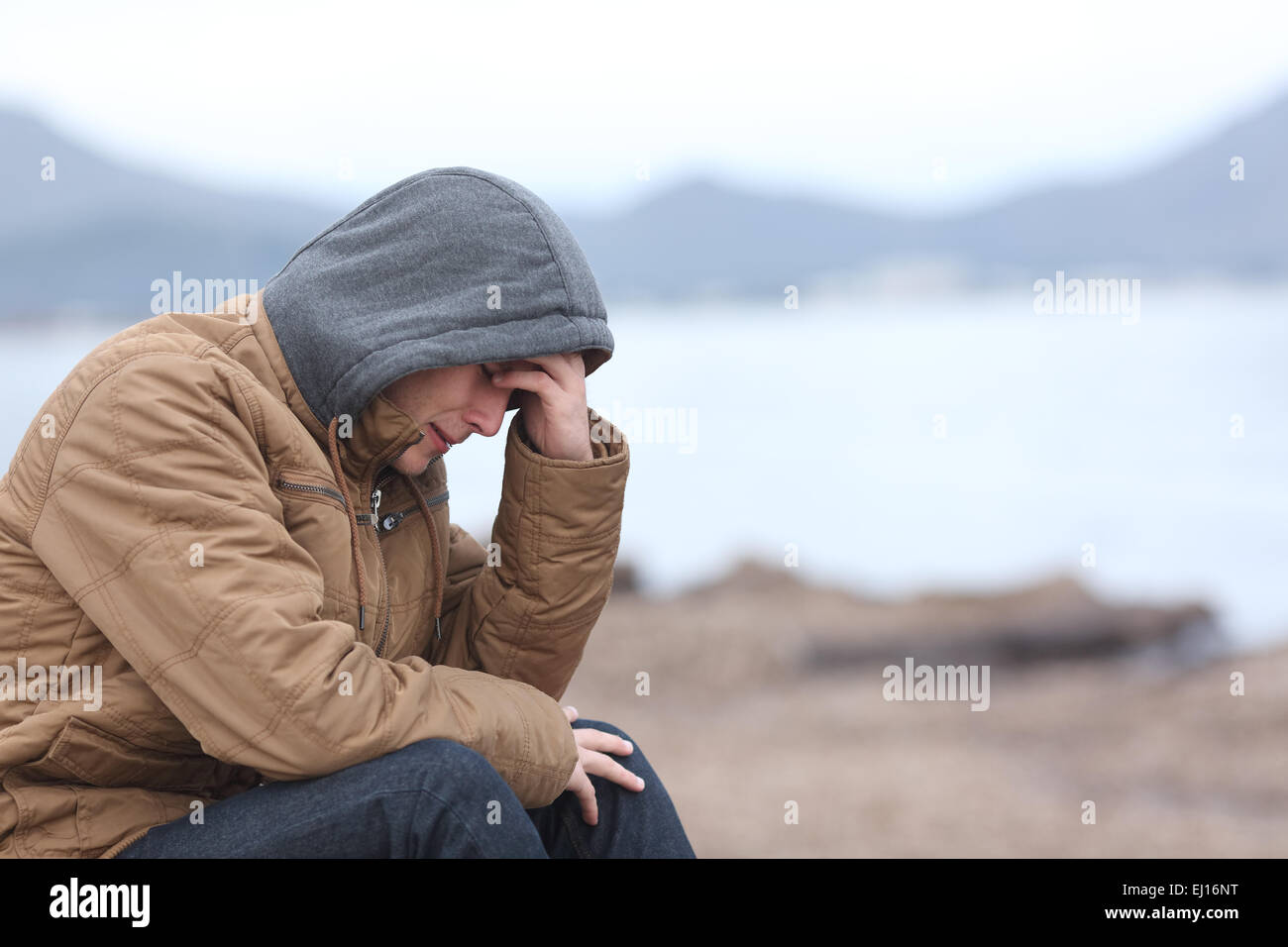 Worried teenager guy crying on the beach in winter in a bad weather day Stock Photo
