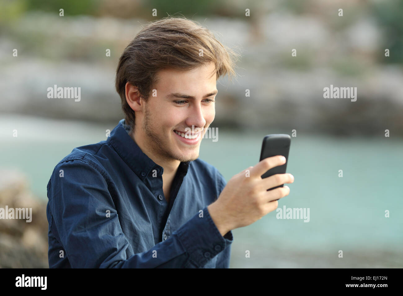 Guy texting on the phone on the beach with the sea in the background Stock Photo