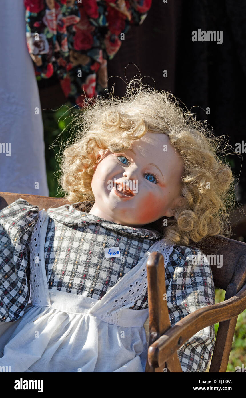 An old doll looks creepy in the morning sun at the August flea market in Gigny-sûr-Saône, Burgundy France Stock Photo