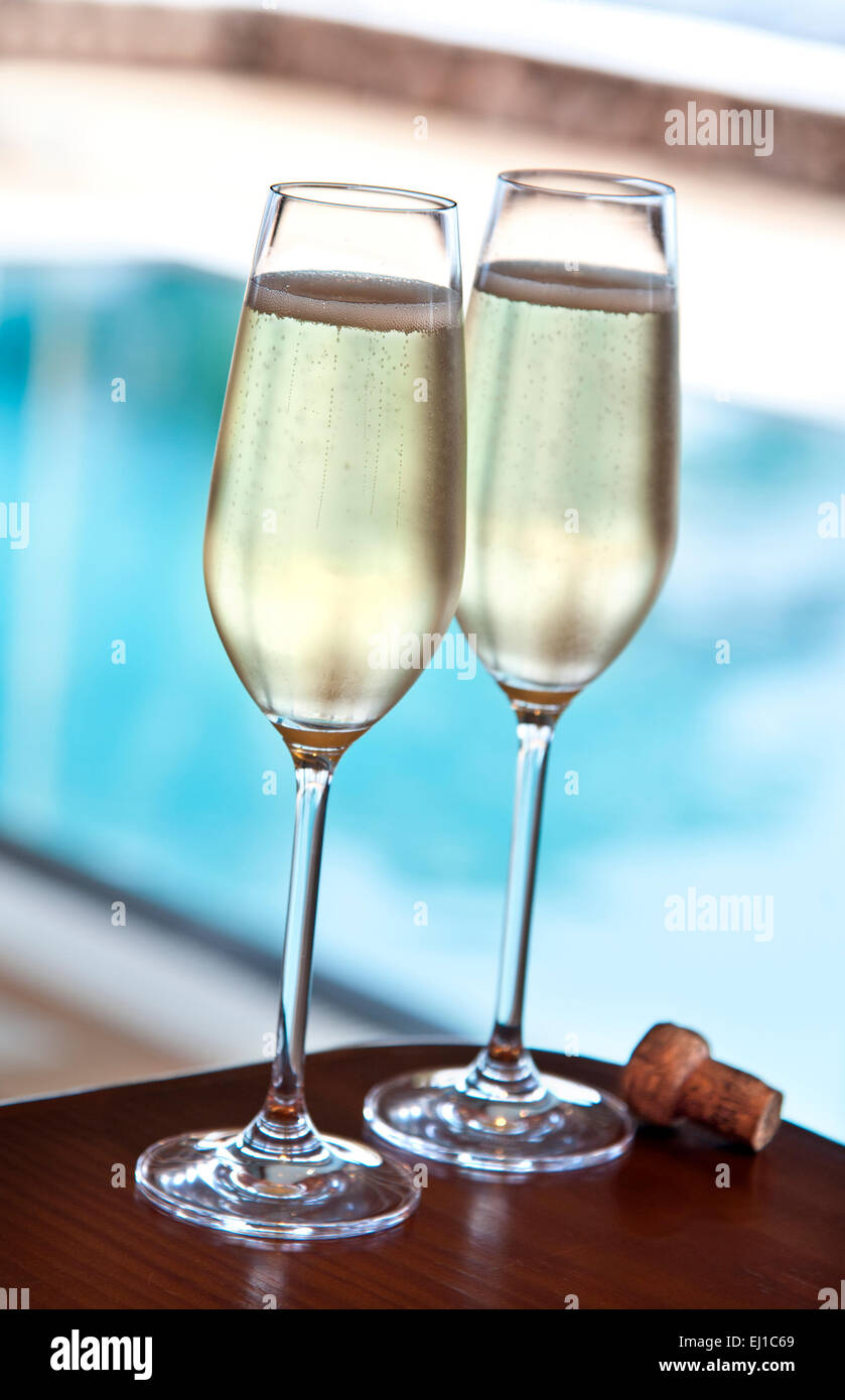 CHAMPAGNE POOL LUXURY Two freshly poured glasses of champagne and cork on alfresco terrace table with luxury infinity swimming pool in background Stock Photo