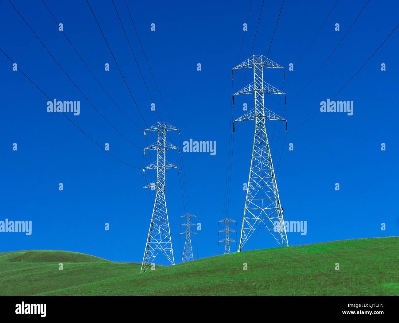Electricity pylons standing on undulating green grass with deep blue sky Stock Photo
