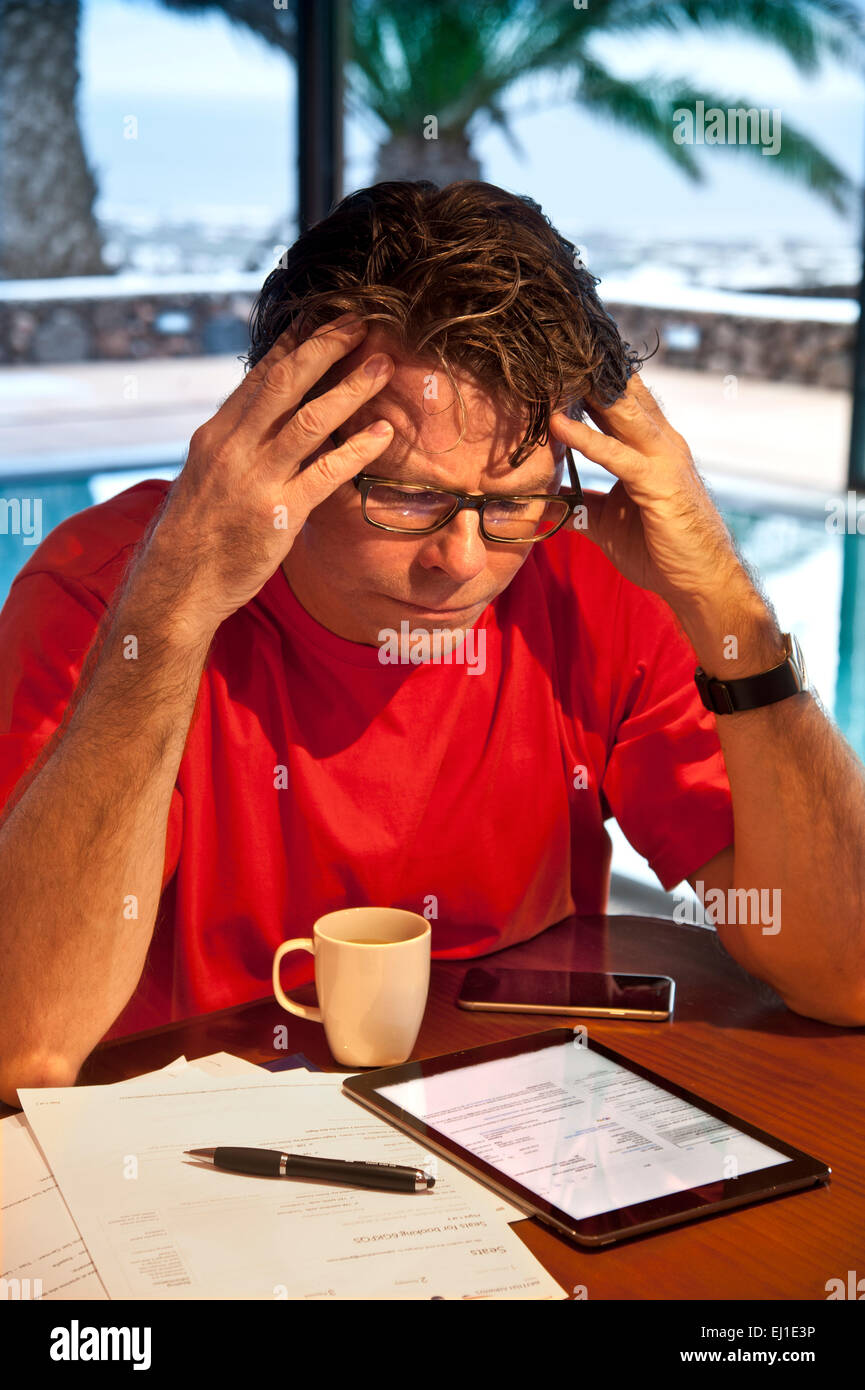 Mature man in holiday setting concentrating on financial statements and business papers along with his iPad Air tablet computer Stock Photo