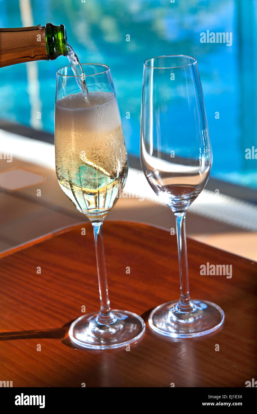SPARKLING WINE POURING Close view on pouring chilled glasses of sparkling champagne wine on sunlit terrace with luxury infinity pool in background Stock Photo