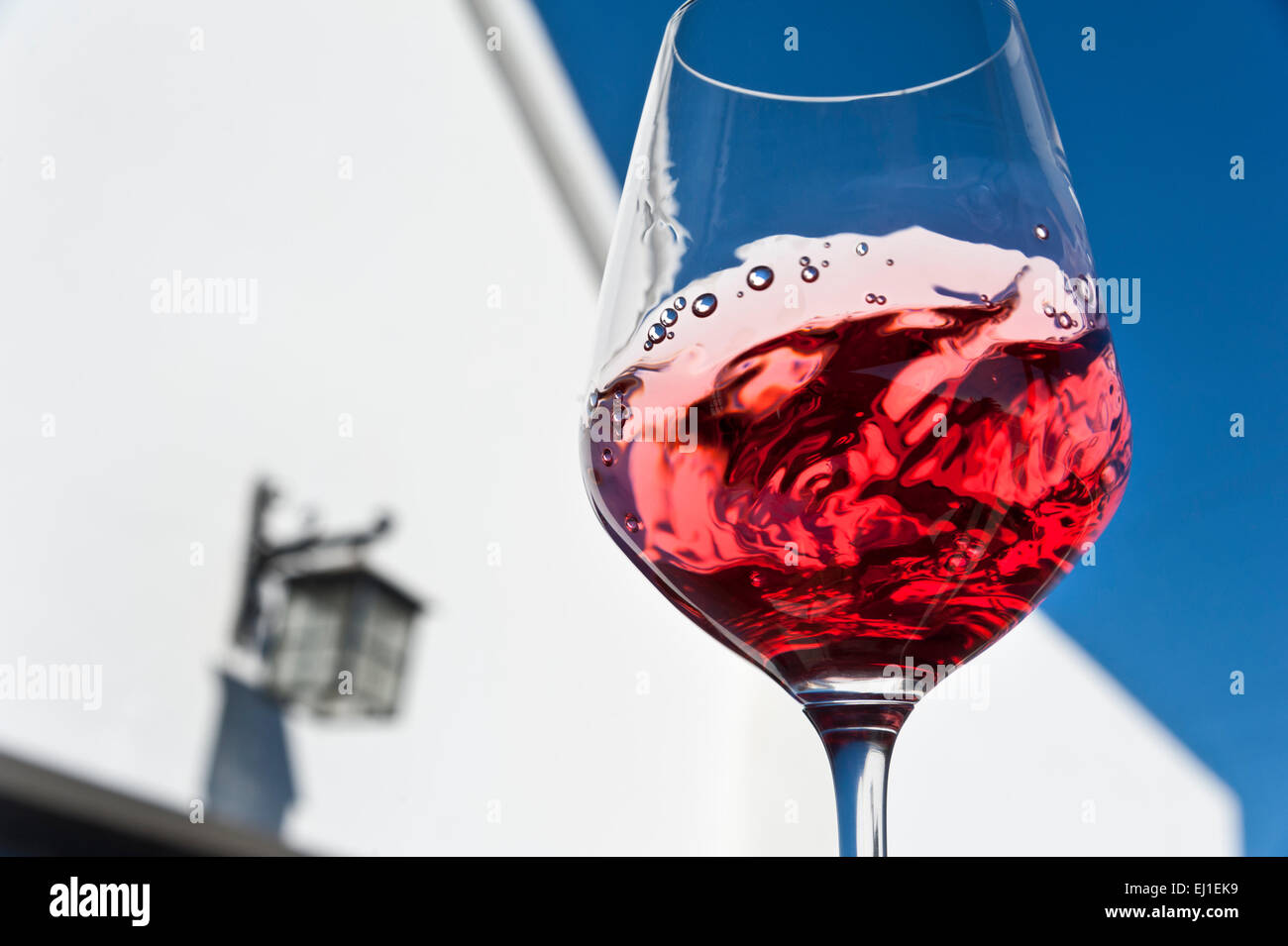 RED WINE TASTING ALFRESCO SUN SKY GRAPHIC  Swirling and evaluating a glass of red wine in outdoor alfresco sunny wine tasting situation Stock Photo