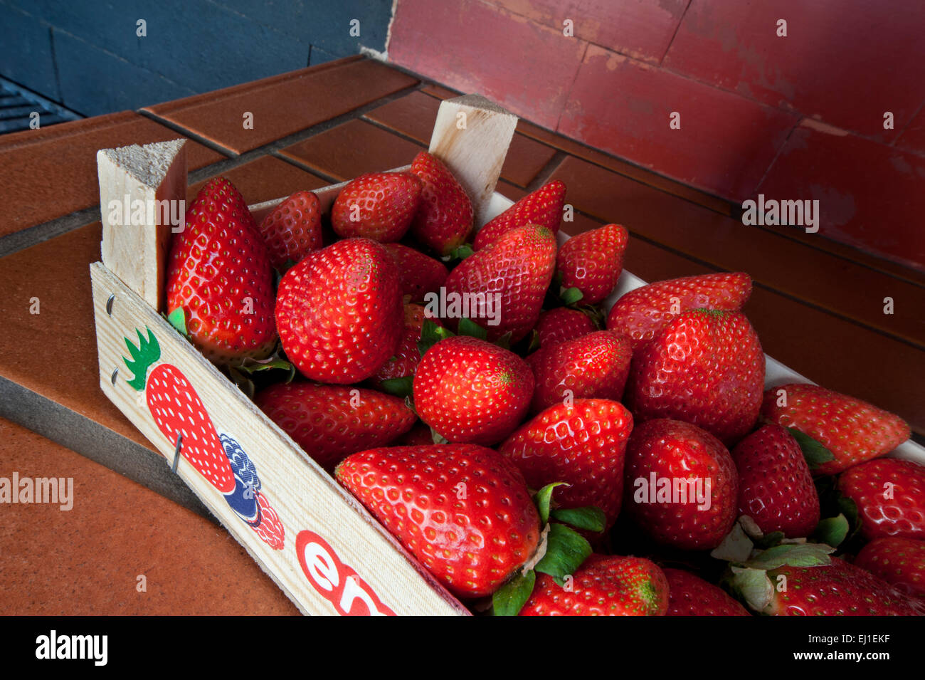 Freshly picked ripe strawberries in wooden crate on alfresco kitchen surface Stock Photo