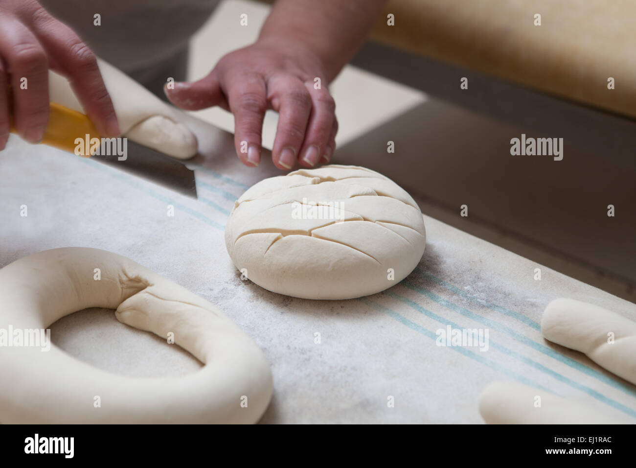 Baker making patterns on raw bread using a cutter to shape the dough