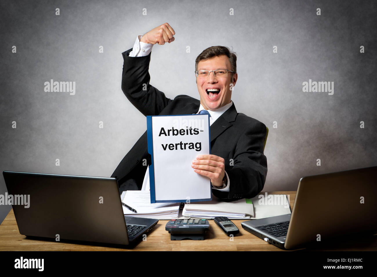 Happy businessman at the office desk is holding a employment contract with german title 'Arbeitsvertrag' Stock Photo