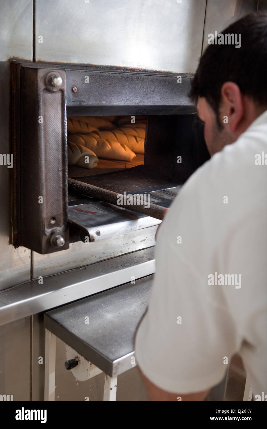 Baker taking fresh baked bread from oven. Manufacturing process of ...