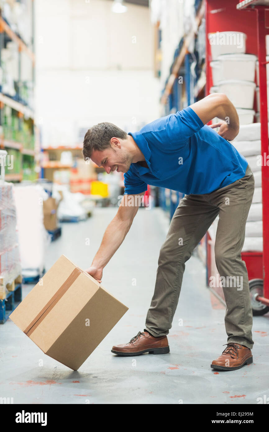 Worker with backache while lifting box in warehouse Stock Photo