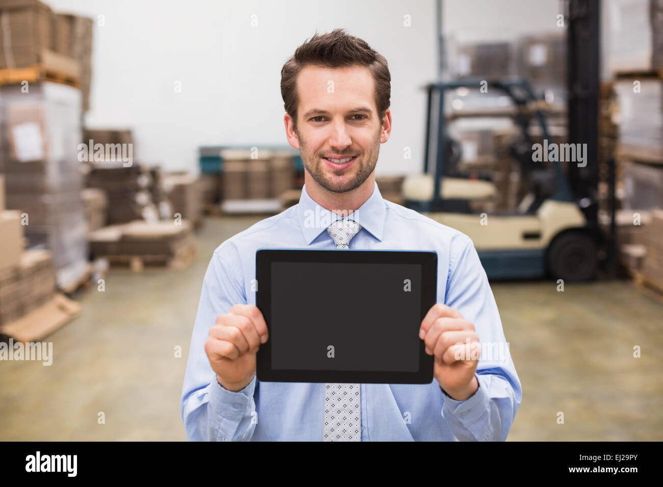 Warehouse manager showing tablet pc smiling at camera Stock Photo