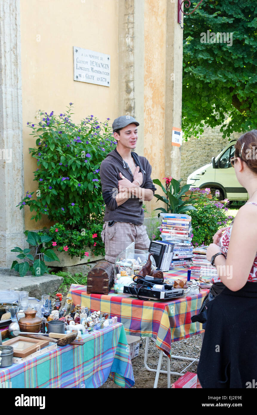 A young man chats with customers at the village marché aux puces in Gigny-sûr-Saône, Burgundy. Stock Photo