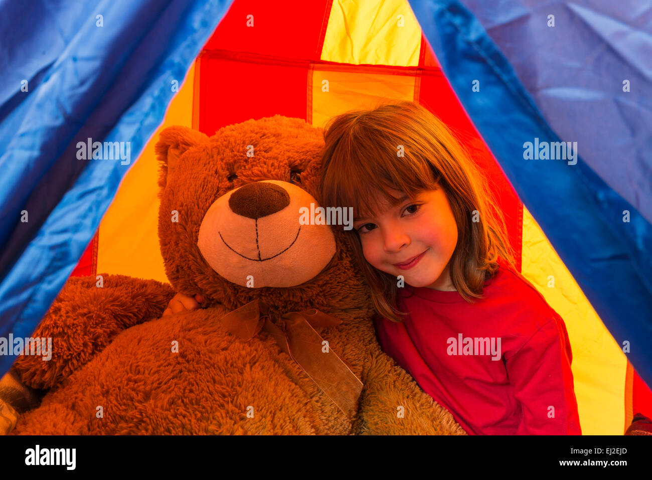 Little girl hugging her big teddy bear looking at camera inside a tent