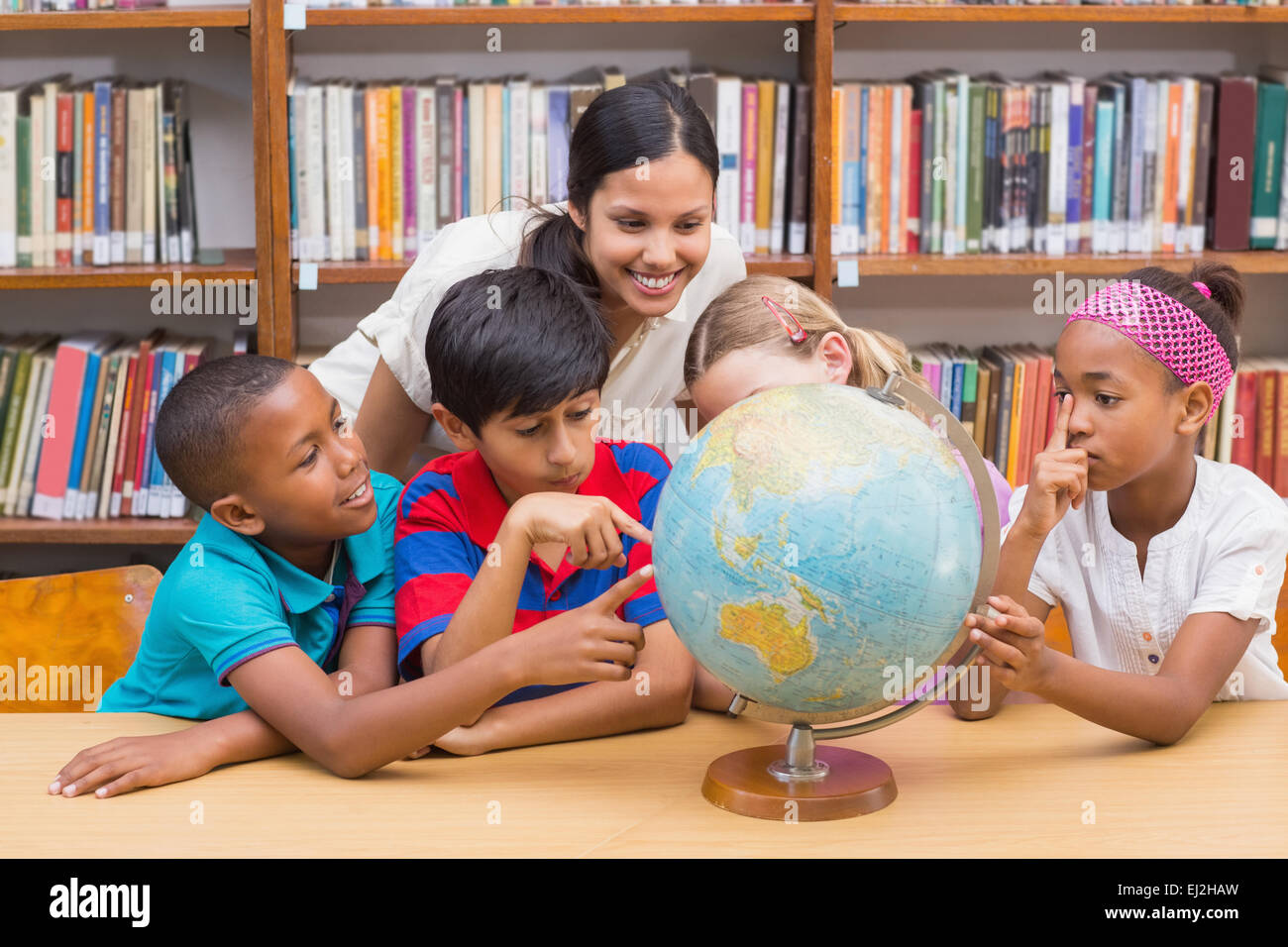 Cute pupils and teacher looking at globe in library Stock Photo - Alamy