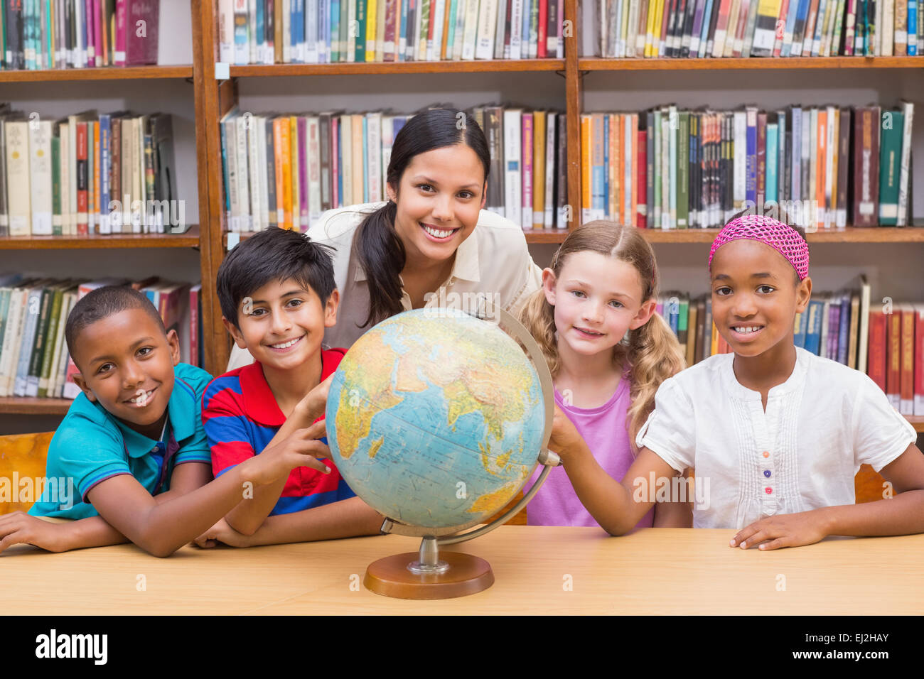 Cute pupils and teacher looking at globe in library Stock Photo - Alamy