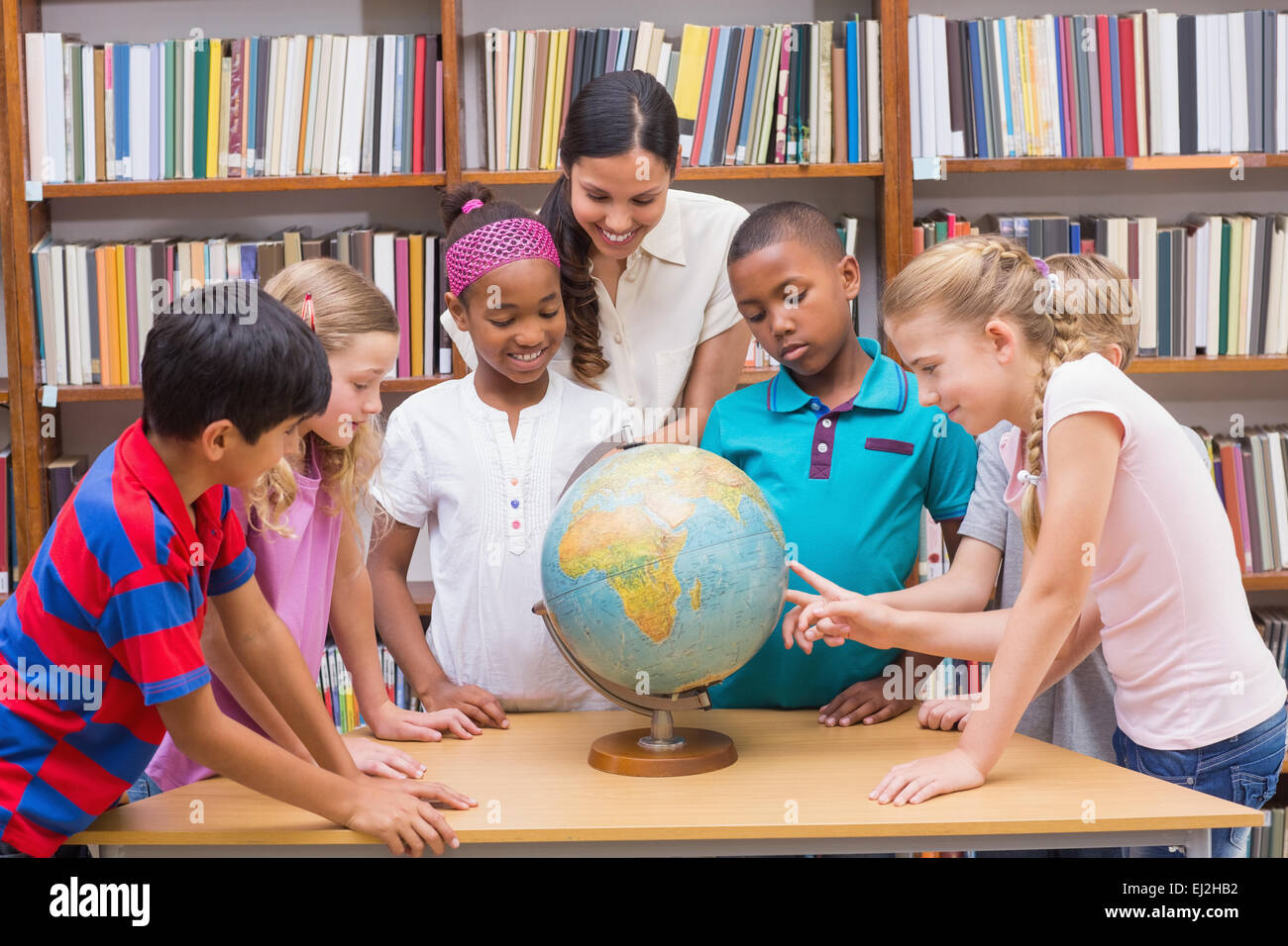 Cute pupils and teacher looking at globe in library Stock Photo - Alamy