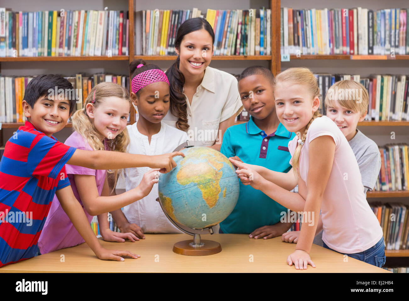 Cute pupils and teacher looking at globe in library Stock Photo - Alamy