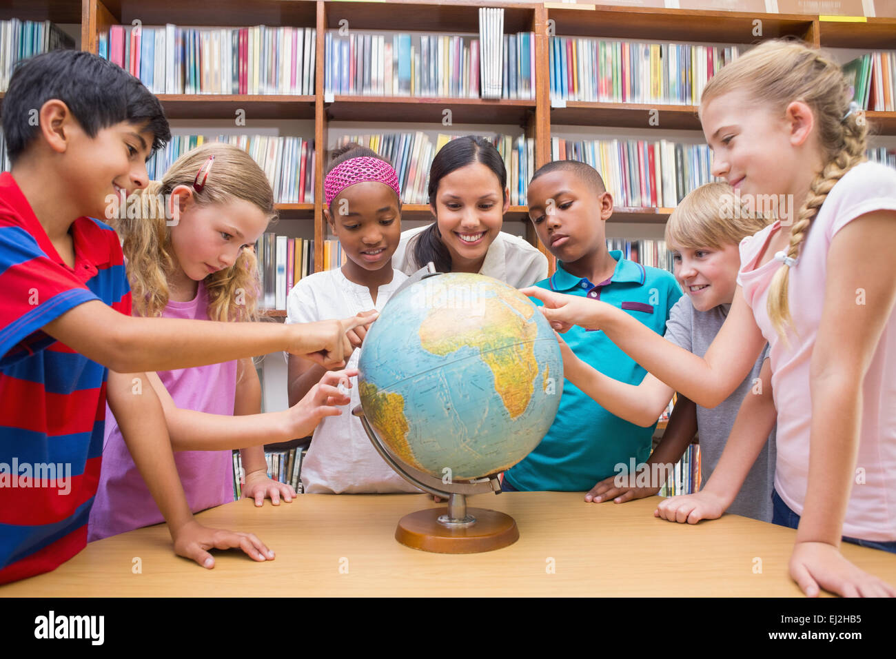 Cute pupils and teacher looking at globe in library Stock Photo - Alamy