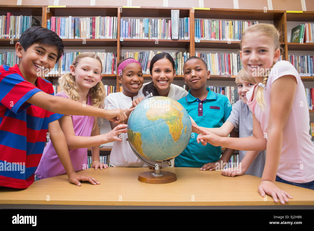 Cute pupils and teacher looking at globe in library Stock Photo - Alamy
