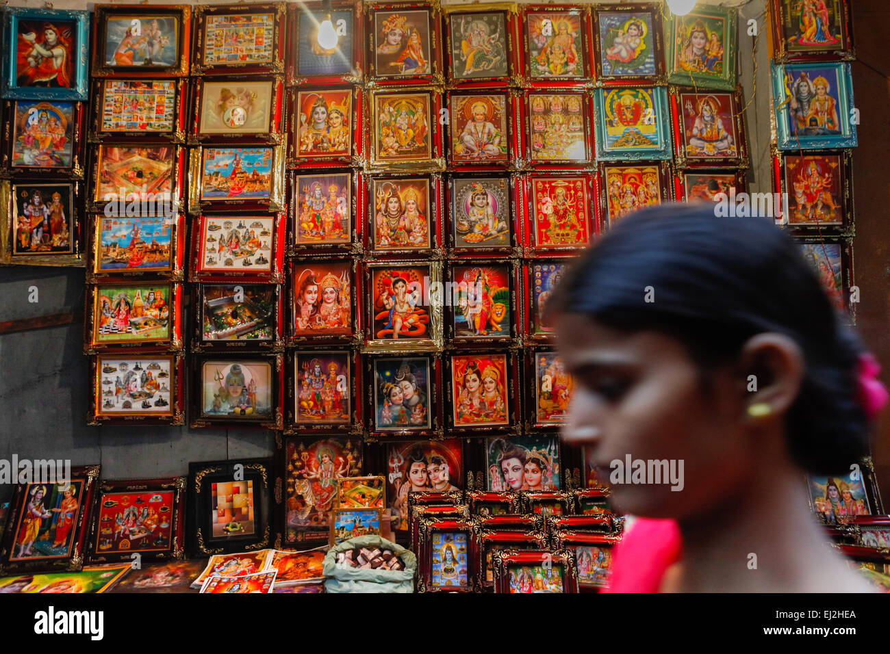 Woman passes in front of gods images shop at one of alleys of Varanasi, India. Stock Photo