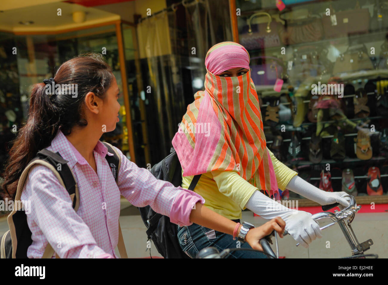 A schoolgirl wearing hijab having a conversation with friend as they are riding bicycles during a traffic jam in Varanasi, Uttar Pradesh, India. Stock Photo