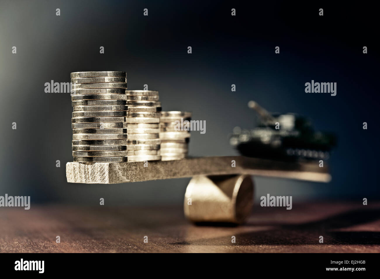 Seesaw with stacks of coins on one side and a tank on the other side. Stock Photo