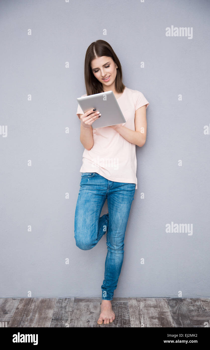 Young woman using tablet computer and leaning on the gray wall Stock Photo