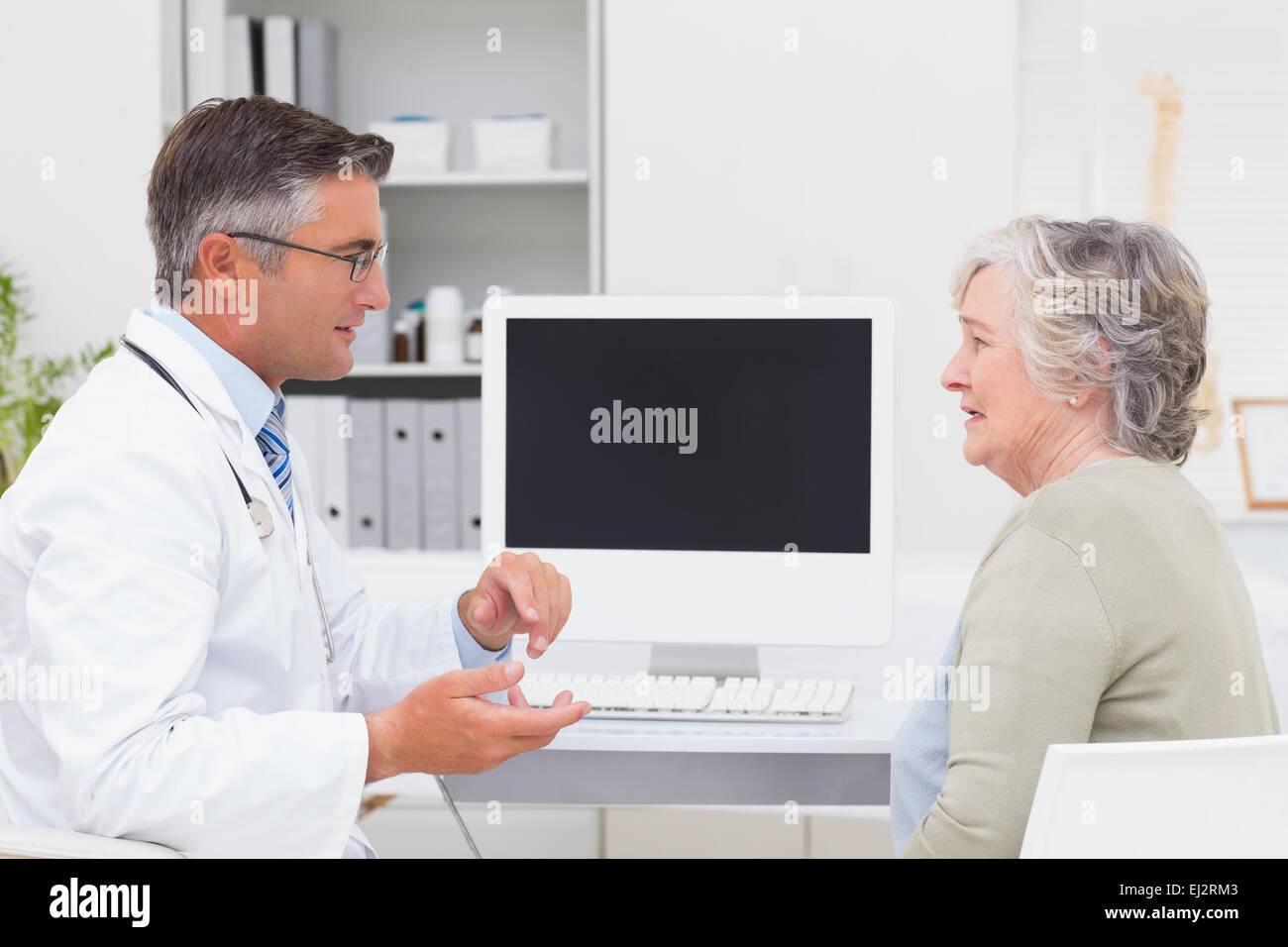 Male doctor conversing with senior patient at table Stock Photo