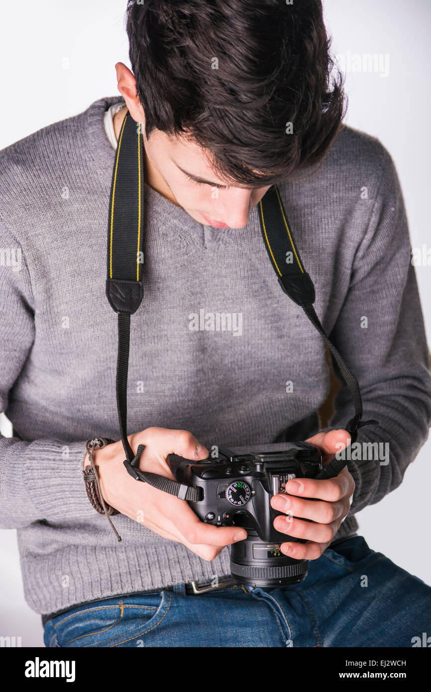 Handsome young male photographer looking at photographs on his professional photo camera's display hanging from his neck, isolat Stock Photo