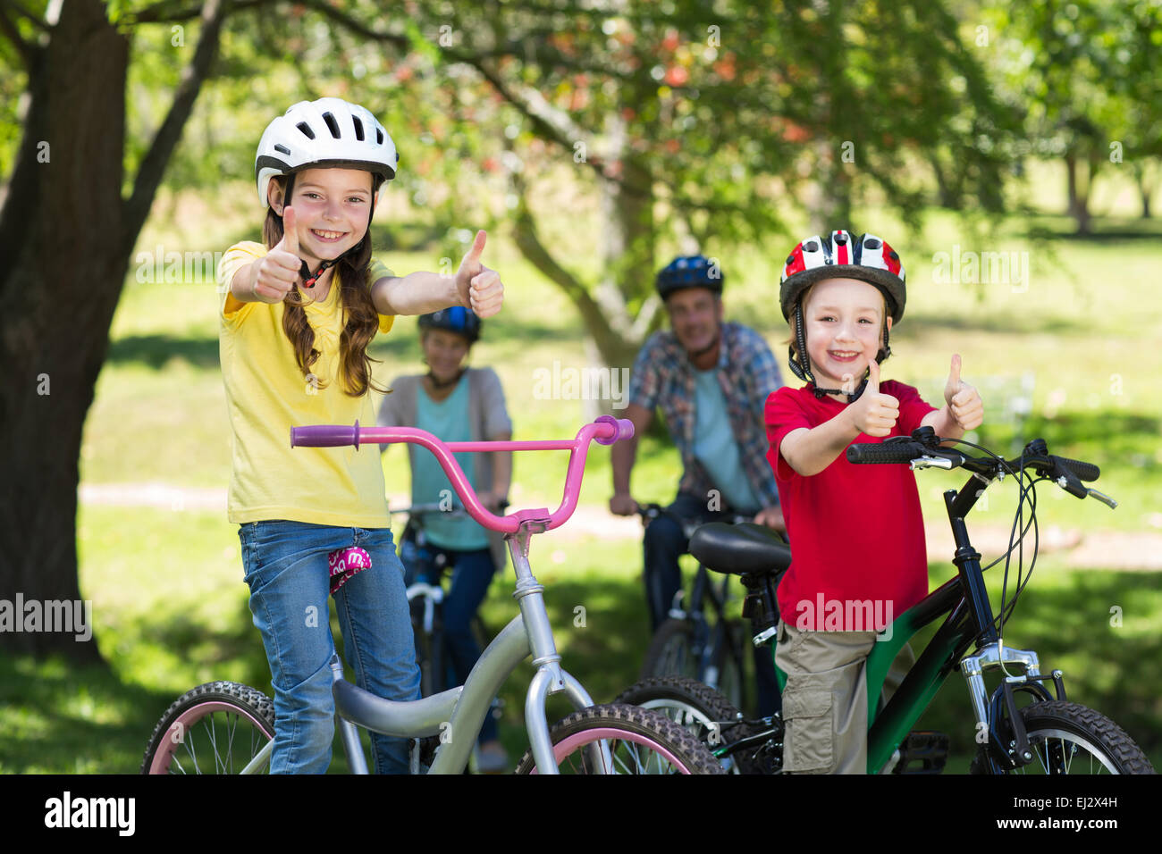 Happy family on their bike at the park with thumbs up Stock Photo