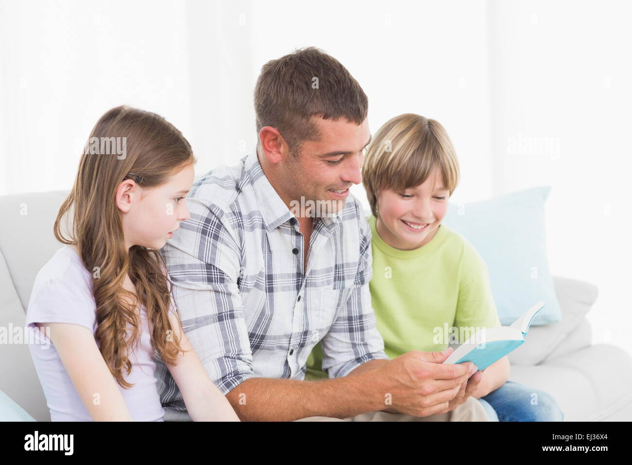 Man telling story to children while sitting on sofa Stock Photo