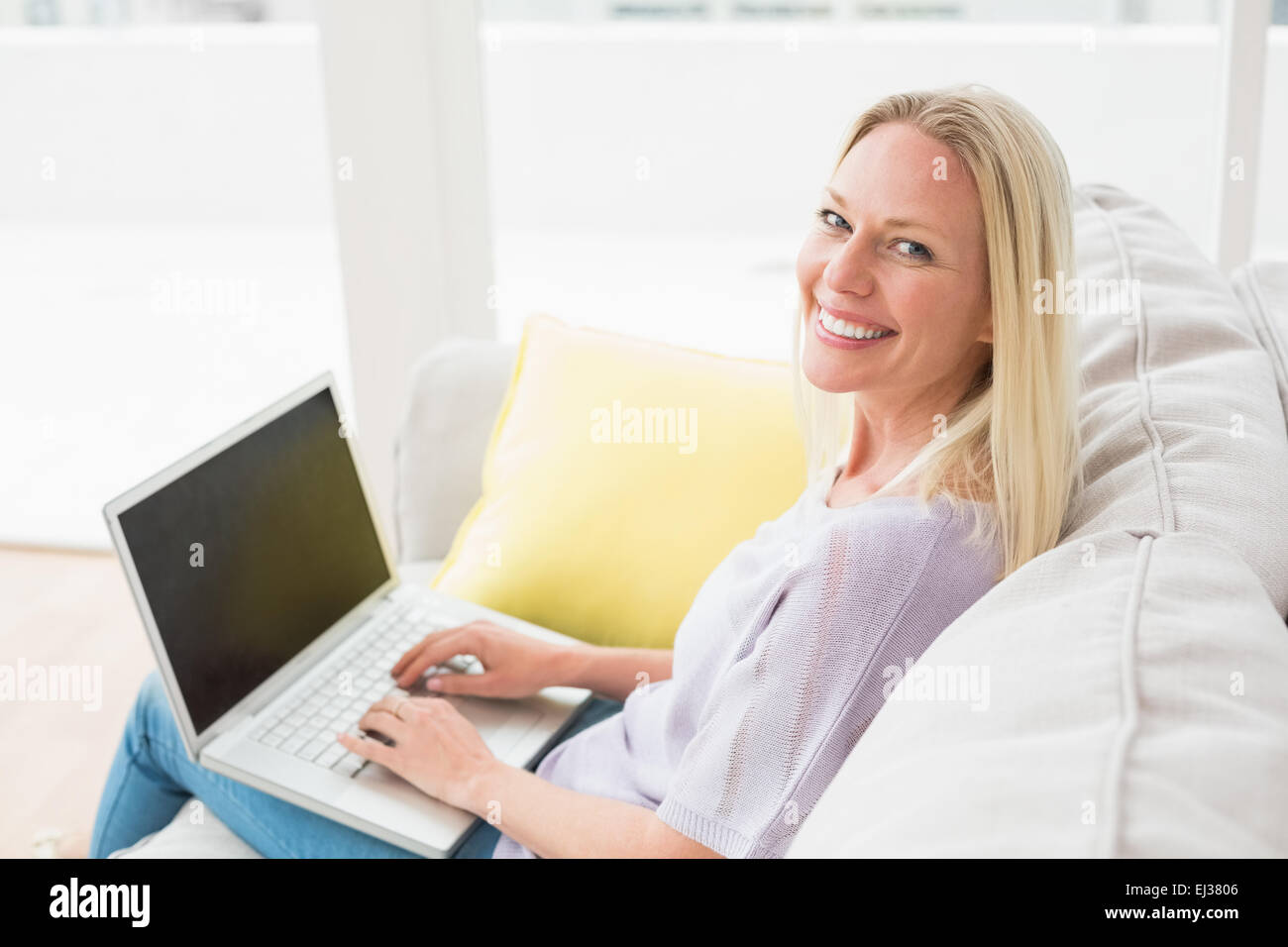 Smiling woman on sofa using laptop in living room Stock Photo - Alamy