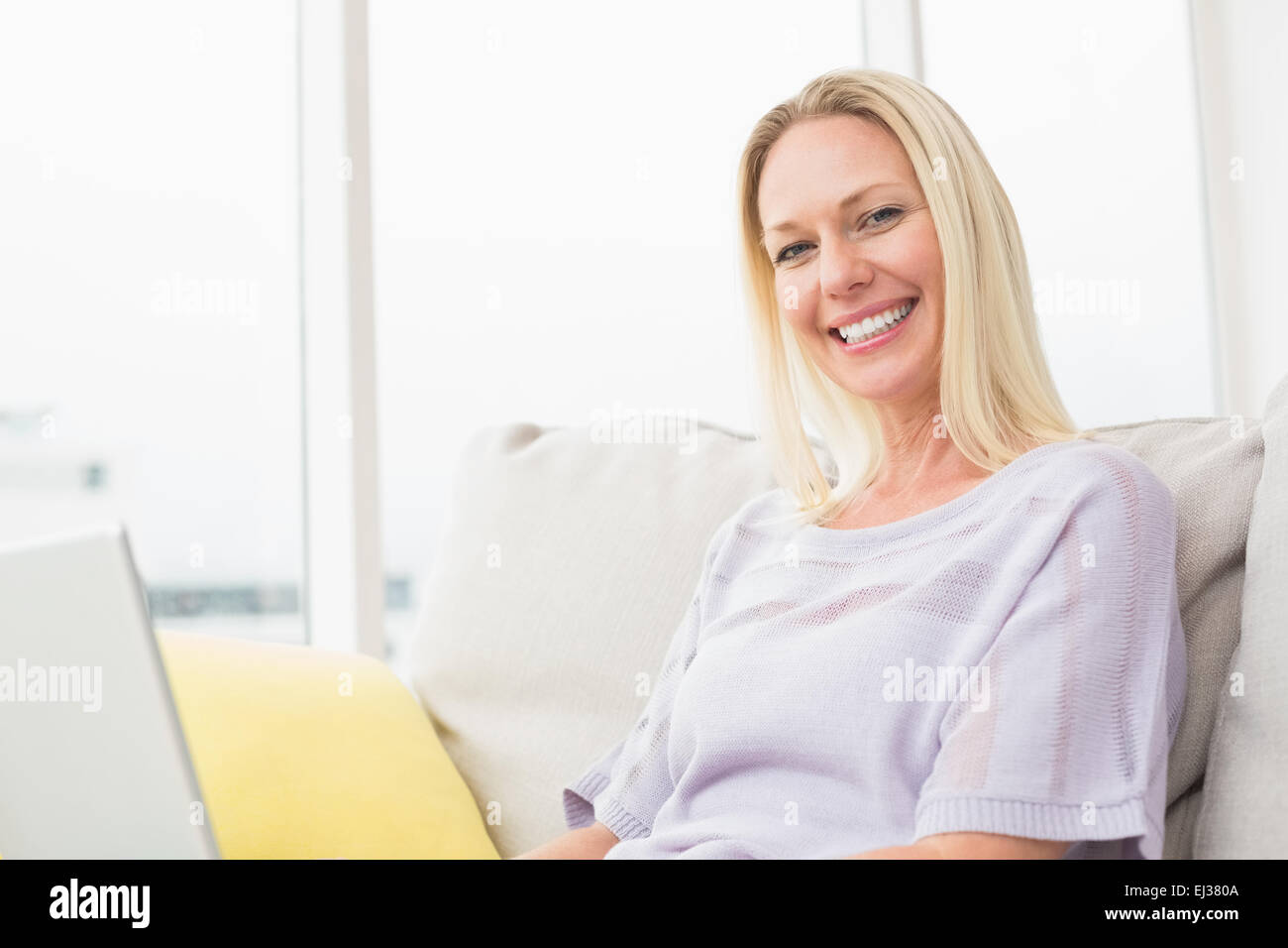 Smiling woman with laptop sitting on sofa Stock Photo - Alamy
