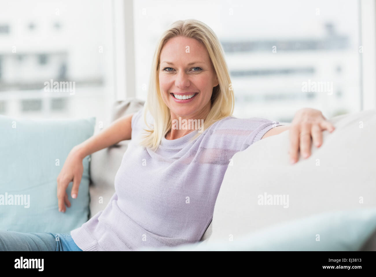 Smiling woman sitting on sofa in living room Stock Photo - Alamy