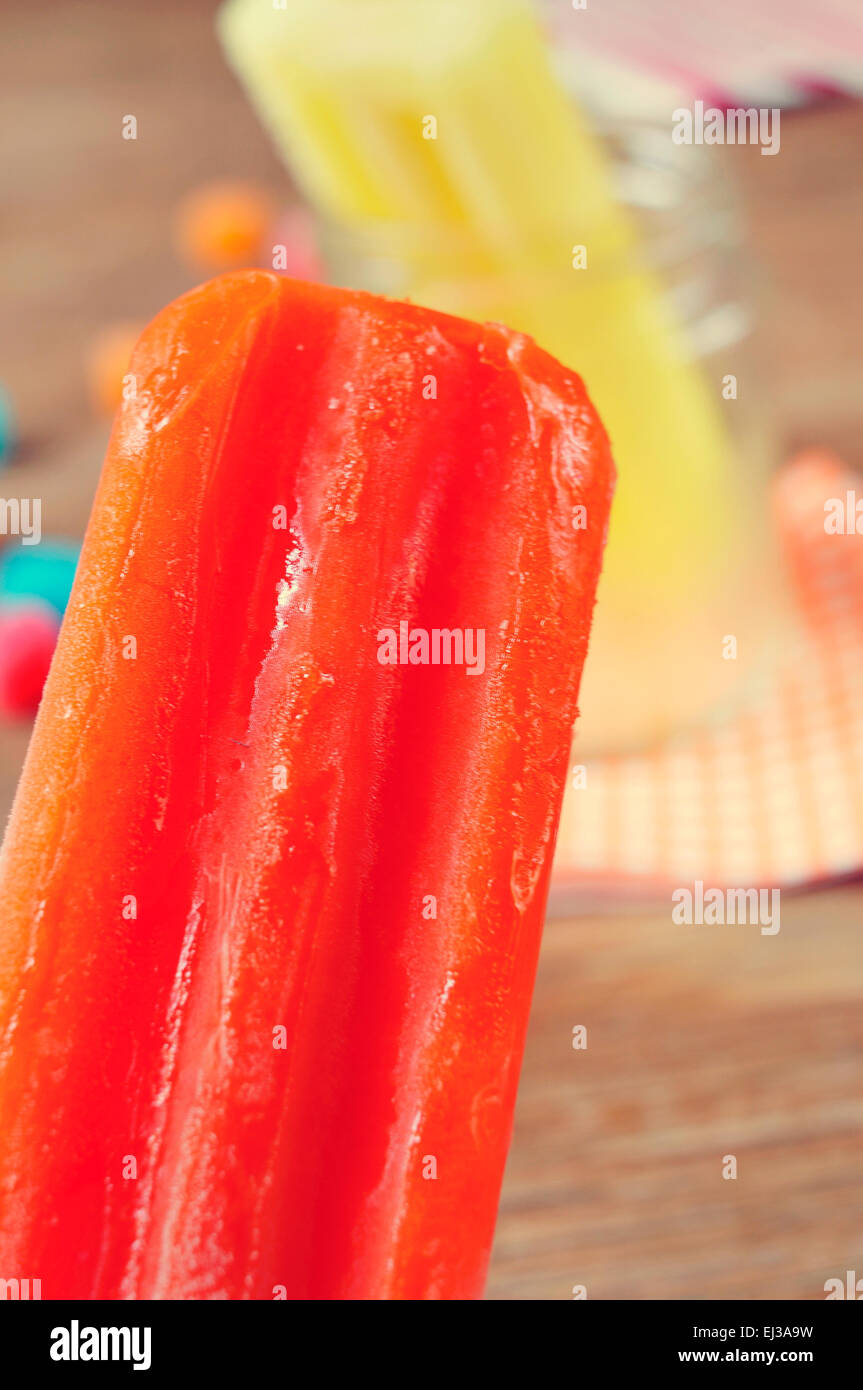 closeup of an appetizing orange flavored ice pop and another one lemon flavored in a glass jar in the background Stock Photo