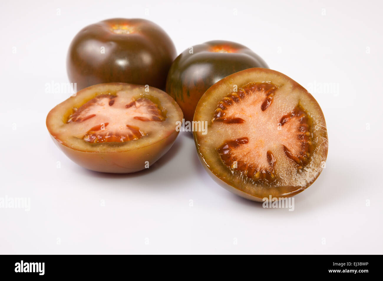 Dark green kumato tomatoes, whole and sliced. Isolated over white