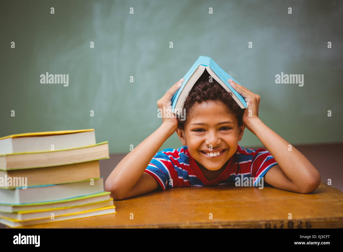 Little boy holding book over head in classroom Stock Photo Alamy