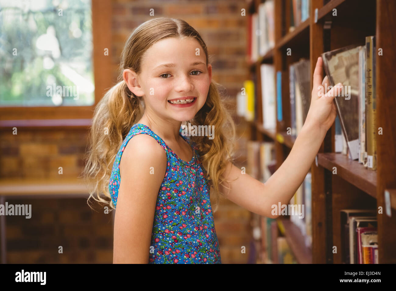 Cute little girl selecting book in library Stock Photo - Alamy
