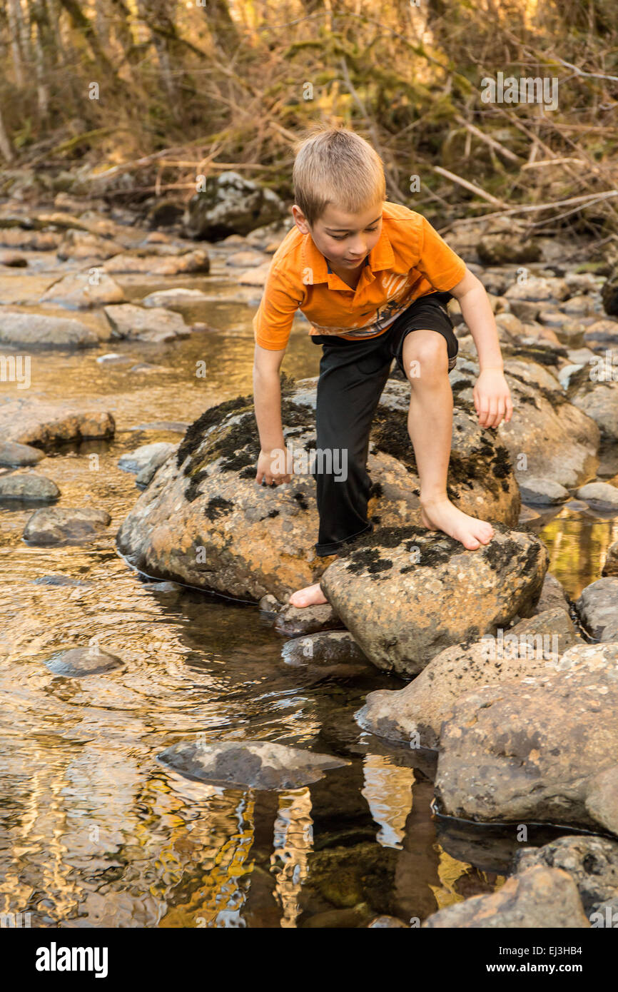 Seven year old barefoot boy climbing on rocks in the Snoqualmie River near North Bend, Washington, USA Stock Photo