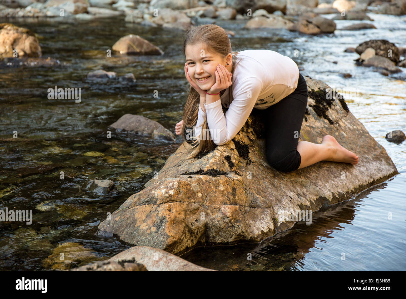 Nine year old girl playfully 'riding a rock' in the Snoqualmie River, in Olallie State Park, near North Bend, Washington, USA Stock Photo