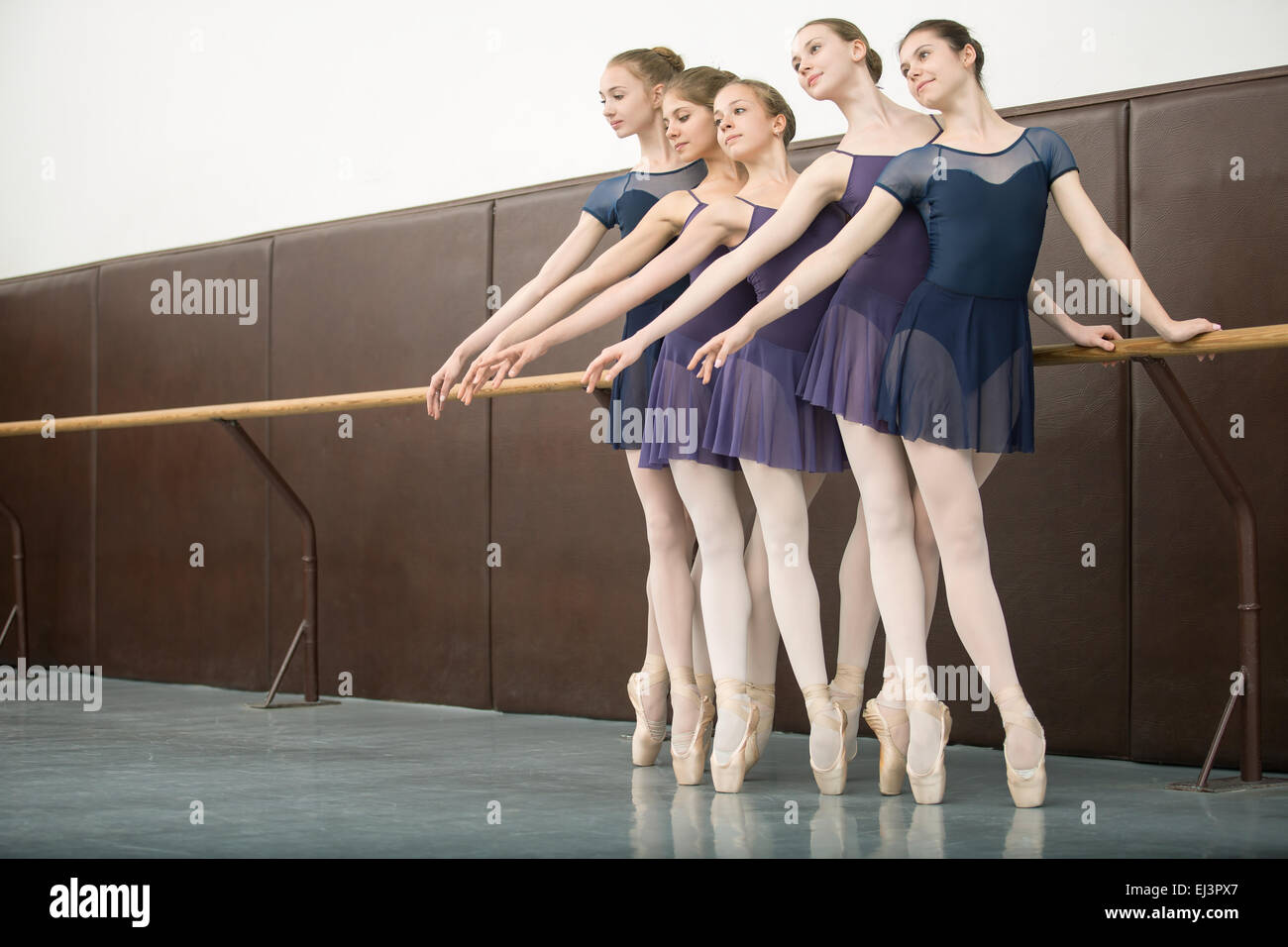 Five ballet dancers in class near the barre. Model wearing white Stock