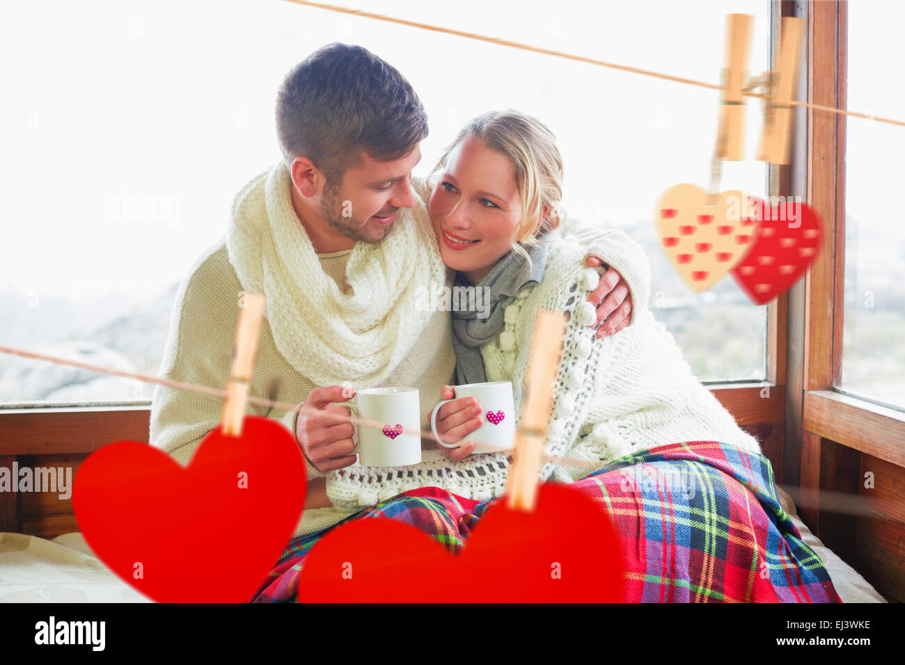 Composite image of loving couple in winter wear with cups against window Stock Photo